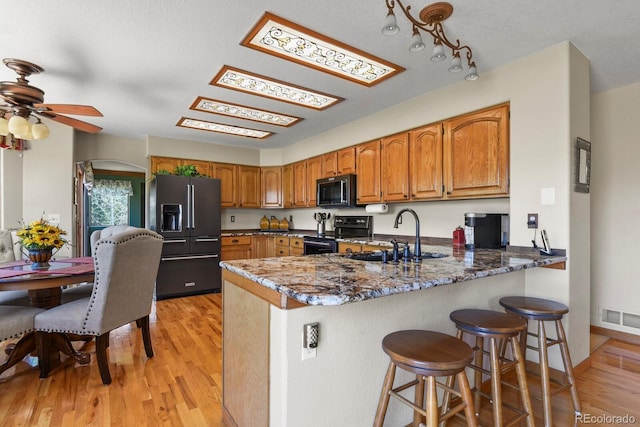kitchen with a peninsula, a sink, brown cabinetry, visible vents, and black appliances