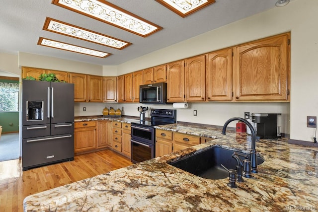 kitchen with a sink, stone countertops, brown cabinetry, appliances with stainless steel finishes, and light wood-style floors