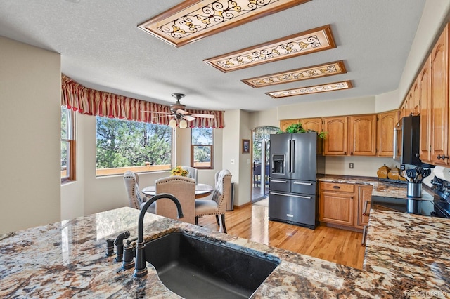 kitchen with light wood finished floors, dark stone countertops, a sink, brown cabinetry, and high end refrigerator