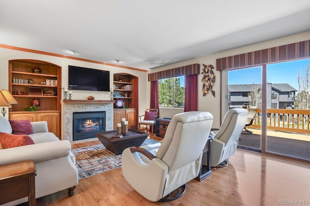 living room featuring light wood finished floors, built in features, and a glass covered fireplace