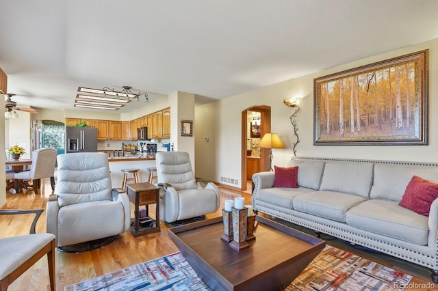 living room featuring light wood-style floors, visible vents, a ceiling fan, and arched walkways