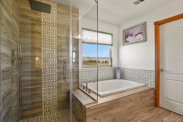 bathroom featuring a bath, visible vents, wood finished floors, and a tile shower
