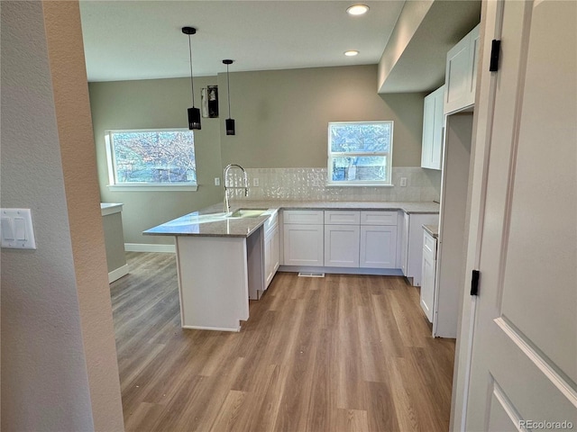 kitchen with kitchen peninsula, sink, decorative backsplash, decorative light fixtures, and white cabinetry