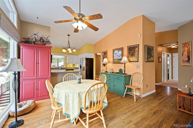 dining area with high vaulted ceiling, ceiling fan with notable chandelier, and light hardwood / wood-style floors