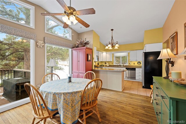 dining area with high vaulted ceiling, ceiling fan with notable chandelier, and light hardwood / wood-style floors