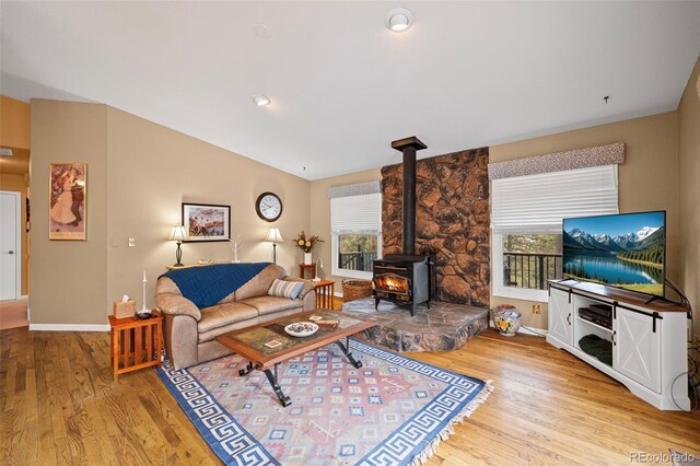 living room with light hardwood / wood-style flooring, a wealth of natural light, vaulted ceiling, and a wood stove