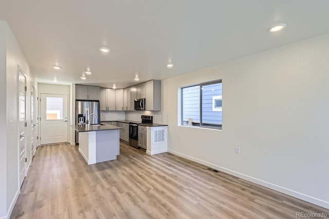 kitchen featuring sink, gray cabinetry, light hardwood / wood-style flooring, a center island with sink, and appliances with stainless steel finishes