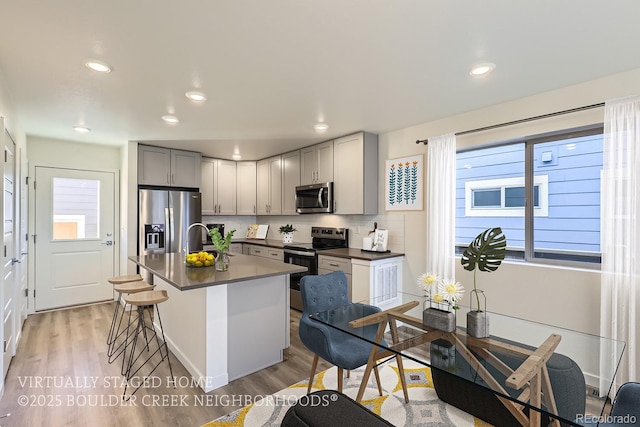 kitchen featuring tasteful backsplash, an island with sink, gray cabinetry, light hardwood / wood-style floors, and stainless steel appliances