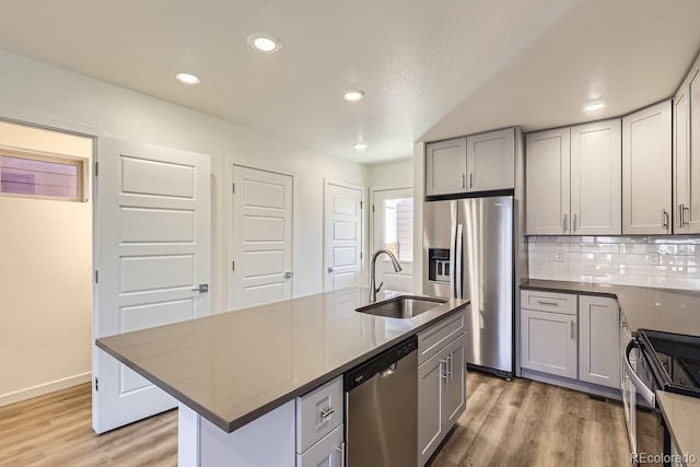 kitchen with an island with sink, appliances with stainless steel finishes, sink, and gray cabinetry