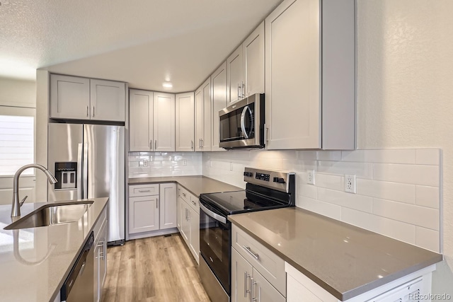 kitchen featuring appliances with stainless steel finishes, sink, dark stone countertops, decorative backsplash, and light hardwood / wood-style floors