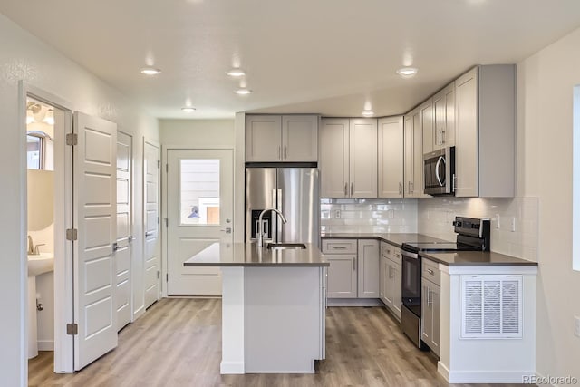 kitchen with sink, a center island with sink, light hardwood / wood-style flooring, gray cabinets, and stainless steel appliances