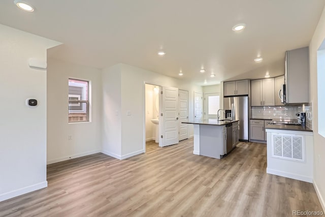 kitchen with gray cabinetry, light hardwood / wood-style flooring, an island with sink, stainless steel appliances, and backsplash