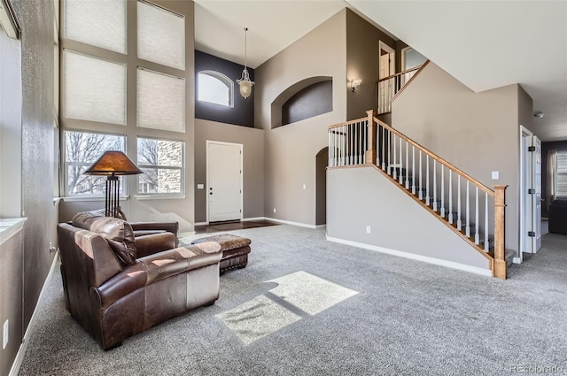 living area featuring carpet flooring, baseboards, a high ceiling, and stairs