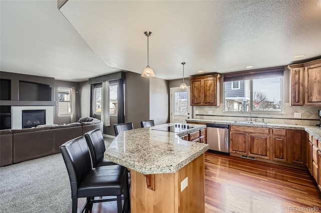 kitchen featuring dishwasher, brown cabinets, a center island, black electric cooktop, and a kitchen bar