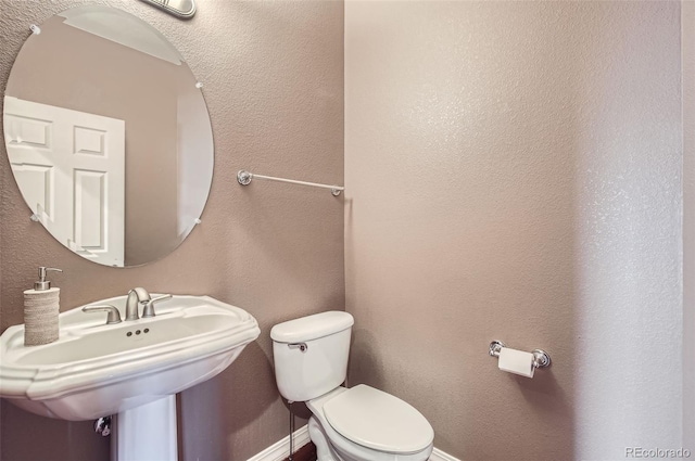 bathroom featuring a textured wall, a sink, toilet, and baseboards