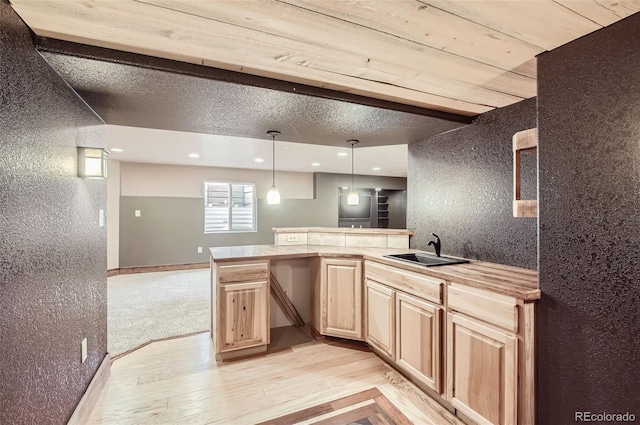 kitchen with light countertops, light wood-style floors, light brown cabinets, a sink, and a peninsula