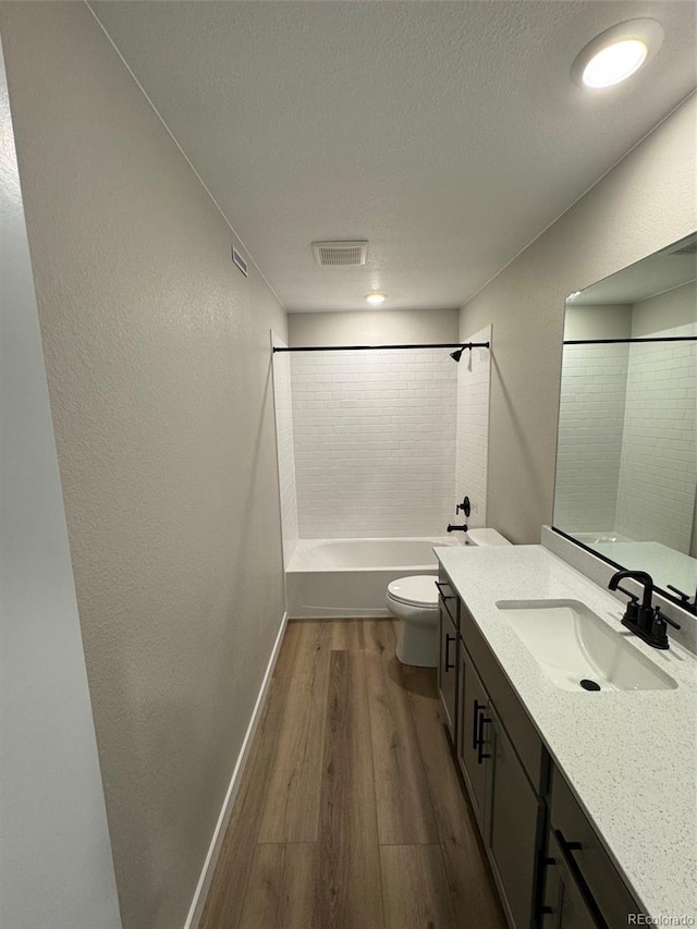 full bathroom featuring toilet, wood-type flooring, a textured ceiling, vanity, and tiled shower / bath combo