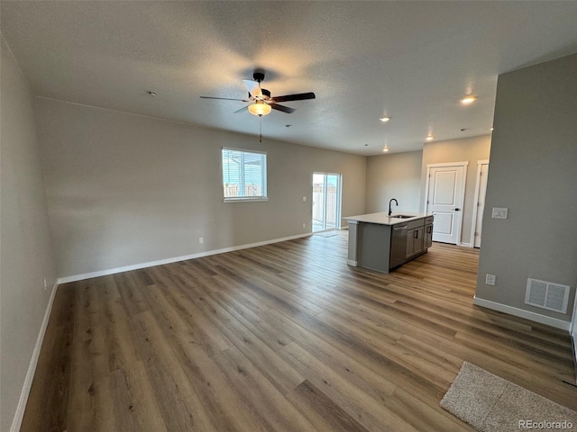 unfurnished living room featuring hardwood / wood-style flooring, ceiling fan, sink, and a textured ceiling