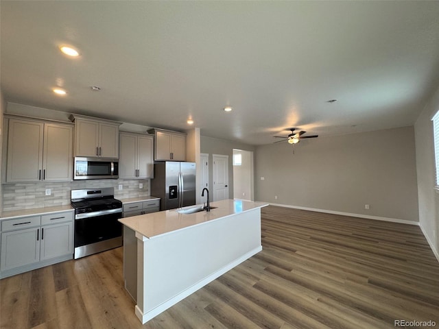 kitchen featuring sink, gray cabinets, appliances with stainless steel finishes, tasteful backsplash, and a center island with sink