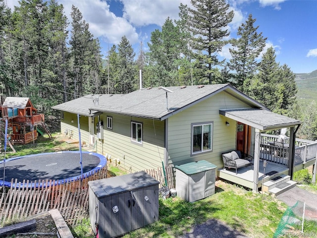 8340 London Ln, Conifer, CO 80433 - rear view of house with a trampoline, a deck, a shingled roof, a playground, and a yard
