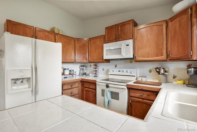 kitchen with white appliances, tile countertops, brown cabinets, a sink, and backsplash