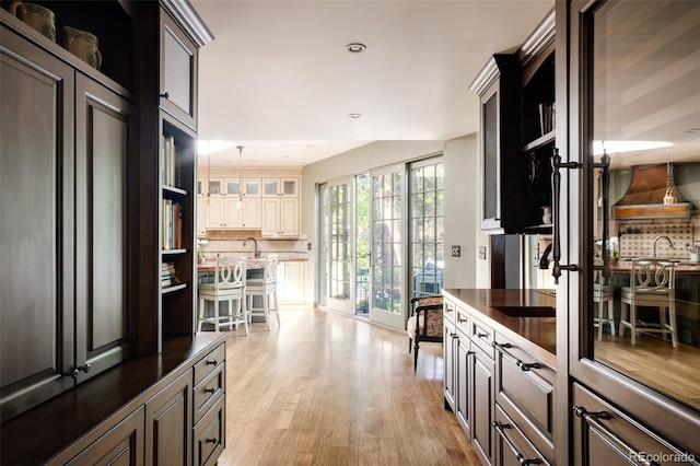 kitchen featuring light hardwood / wood-style floors, pendant lighting, cream cabinets, decorative backsplash, and wall chimney range hood