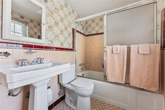 bathroom featuring toilet, shower / bath combination with glass door, and tile walls