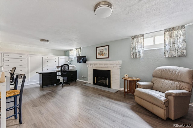 office space with a brick fireplace, light hardwood / wood-style flooring, and a textured ceiling