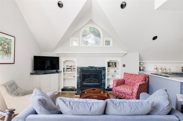 living room featuring hardwood / wood-style flooring, vaulted ceiling, built in features, and a high end fireplace