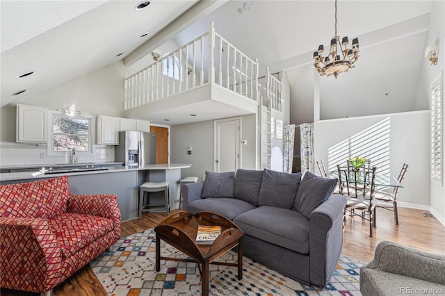 living room featuring a notable chandelier, light hardwood / wood-style flooring, high vaulted ceiling, and plenty of natural light