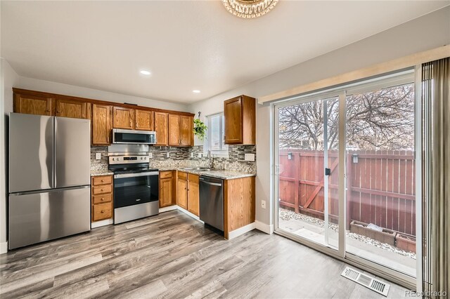 kitchen with stainless steel appliances, sink, decorative backsplash, and light hardwood / wood-style flooring