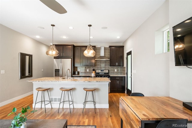 2645 W 24th Ave, Denver, CO 80211 - kitchen featuring wall chimney exhaust hood, appliances with stainless steel finishes, an island with sink, a kitchen breakfast bar, and decorative backsplash