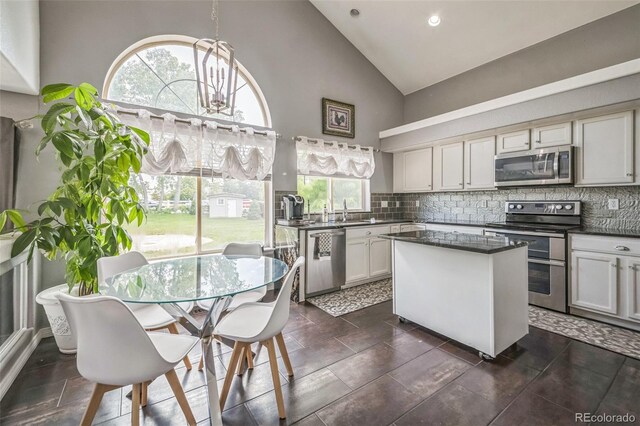 20338 E 48th Dr, Denver, CO 80249 - kitchen featuring appliances with stainless steel finishes, high vaulted ceiling, dark countertops, decorative backsplash, and a center island