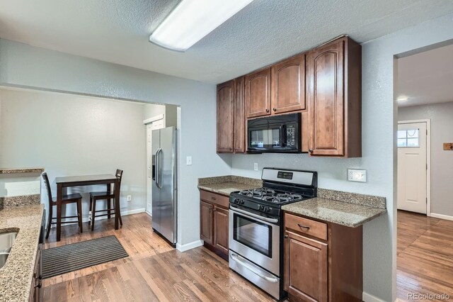 921 Dakin St, Denver, CO 80221 - kitchen with appliances with stainless steel finishes, light wood-type flooring, a textured ceiling, and light stone counters