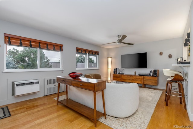 living room featuring a wall mounted AC, ceiling fan, radiator heating unit, and light wood-type flooring