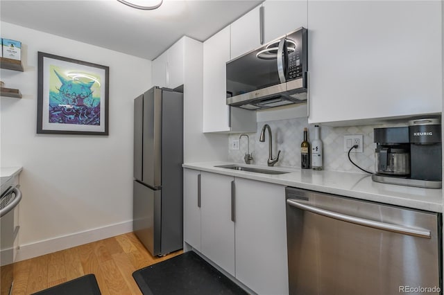 kitchen featuring backsplash, white cabinets, sink, appliances with stainless steel finishes, and light hardwood / wood-style floors