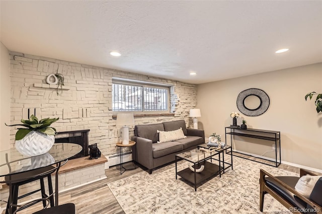 living room featuring a fireplace, light hardwood / wood-style flooring, a textured ceiling, and a baseboard heating unit