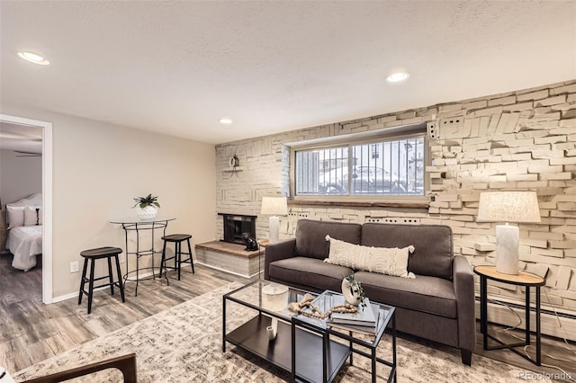 living room with a stone fireplace, wood-type flooring, a baseboard radiator, and a textured ceiling