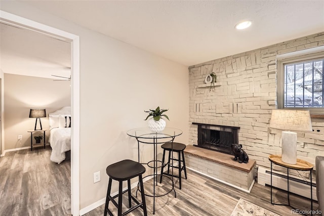 interior space featuring a baseboard radiator, hardwood / wood-style floors, ceiling fan, and a fireplace