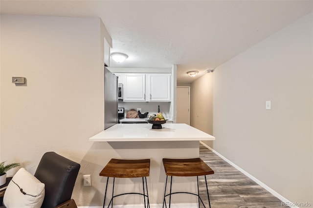 kitchen with appliances with stainless steel finishes, a kitchen breakfast bar, white cabinets, dark hardwood / wood-style flooring, and kitchen peninsula