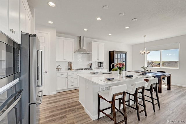 kitchen featuring wall chimney exhaust hood, stainless steel appliances, a sink, light wood-style flooring, and white cabinetry