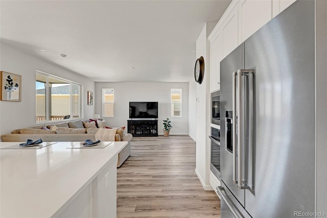 kitchen featuring appliances with stainless steel finishes, white cabinetry, light wood-style flooring, light countertops, and baseboards