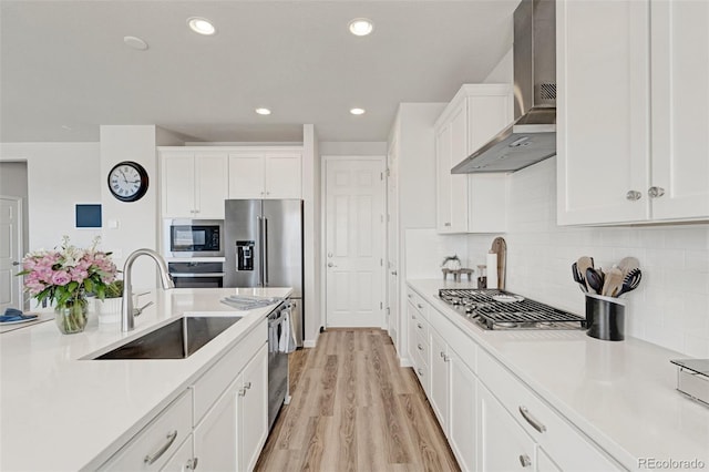 kitchen with wall chimney exhaust hood, a sink, stainless steel appliances, white cabinetry, and light countertops