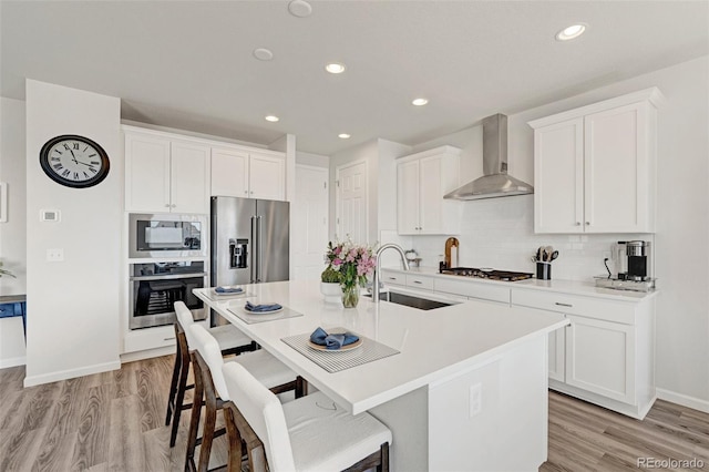 kitchen featuring stainless steel appliances, wall chimney range hood, a sink, a breakfast bar, and recessed lighting