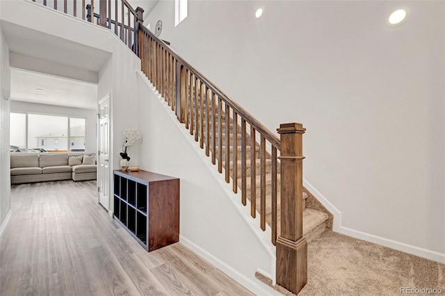 stairway featuring baseboards, wood finished floors, recessed lighting, and a high ceiling