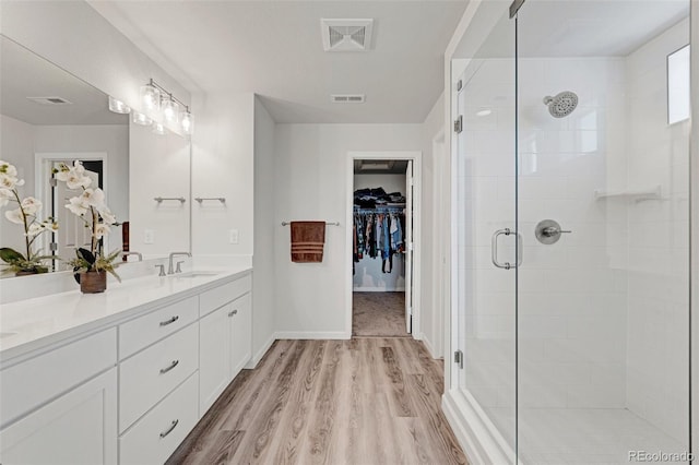 bathroom featuring a stall shower, double vanity, wood finished floors, a spacious closet, and baseboards
