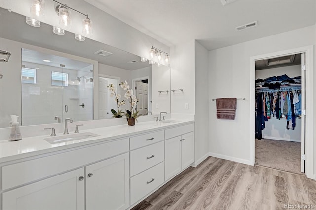 full bath with a shower stall, wood finished floors, double vanity, a spacious closet, and baseboards