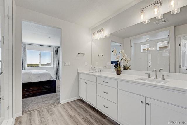 full bath with wood finished floors, a stall shower, connected bathroom, double vanity, and baseboards