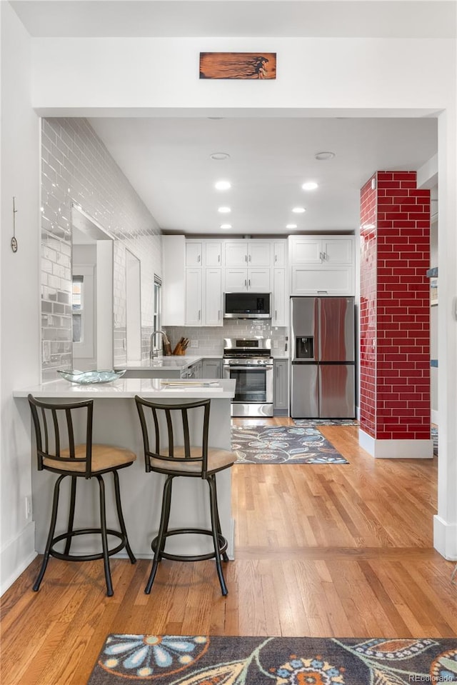 4501 Zenobia St, Denver, CO 80212 - kitchen with appliances with stainless steel finishes, white cabinets, a peninsula, light wood-style flooring, and a breakfast bar