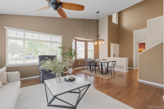 living area featuring baseboards, wood finished floors, ceiling fan, arched walkways, and a towering ceiling